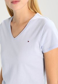 Jasnoniebieska koszulka V-neck z miękkiej bawełny, z krótkimi rękawami, subtelnym logo na klatce piersiowej, gładką teksturą i dopasowanym krojem.