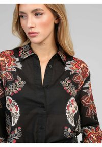 Chemise noire à boutons avec des motifs floraux rouge, gris et crème. Dotée d'un col classique et de manches longues, elle est fabriquée dans un tissu léger.