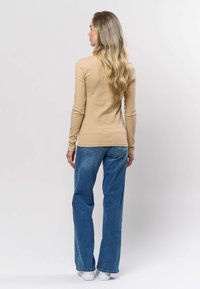 Beige ribbad långärmad topp kombinerad med ljusblå högmidjade, vidbenade jeans och vita sneakers, sedd bakifrån.