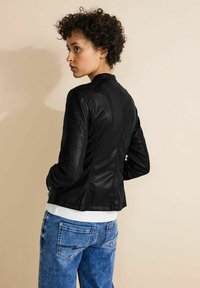Black leather jacket with a fitted design, quilted shoulder accents, and textured detailing, paired with light blue denim jeans.