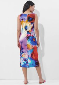 Ärmelloses, knielanges Kleid in lebhaftem, mehrfarbigem abstrakten Muster mit glatter Textur. Mit seitlichem Schlitzdetail, getragen mit flachen rosa Sandalen.
