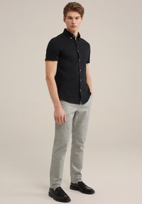 Crna košulja kratkih rukava s dugmetima i kragnom, u kombinaciji sa svijetlo sivo krojenim hlačama i crnim loafers cipelama. Jednostavan, elegantan dizajn.