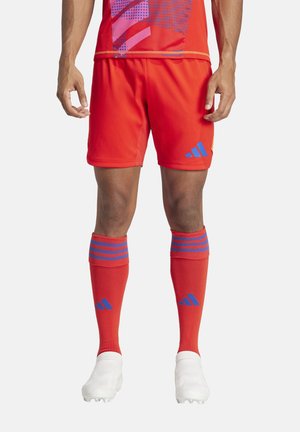 Rode voetbaltenue met een t-shirt met korte mouwen en grafische patronen, bijpassende shorts, kniehoge sokken met blauwe strepen en witte voetbalschoenen.