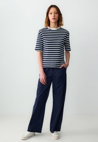 T-shirt à rayures bleu marine et blanches à manches courtes avec un col en forme de coquille, associé à un pantalon bleu marine ample et des baskets blanches.