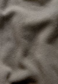 Mīksta, teksturēta auduma materiāls nokrāsots nomierinošā pelēkā krāsā ar viegliem krokām un gludu adījuma rakstu visā virsmā.