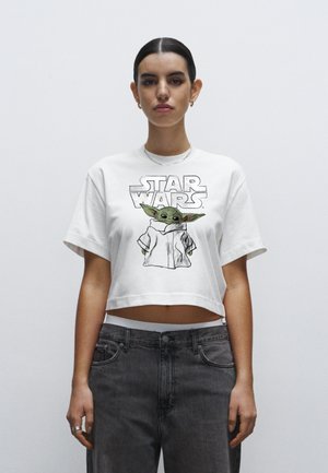 Biały krótki t-shirt z grafiką zielonej postaci o dużych uszach oraz napisem "STAR WARS" w pogrubionym druku.