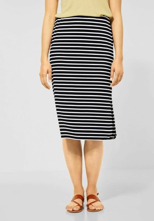 Jupe midi rayée noir et blanc avec un design près du corps, fabriquée en tissu extensible, associée à des sandales en cuir marron.