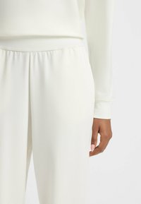 Joggers blancs en tissu lisse avec une taille élastique. Présentent une coupe décontractée et des accents côtelés aux poignets.