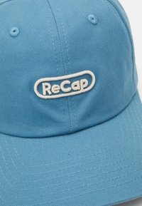 Lyseblå caps laget av teksturert stoff, med en brodert hvit "ReCap"-logo på forsiden. Bøyd skjerm og sydd detaljer.