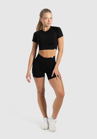 Zwart activewear set bestaande uit een cropped top met korte mouwen en hoge shorts. Gladde textuur met minimale merkdetails.