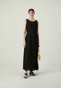 Mustapaita hihaton maksimekko, jossa on istuva yläosa, pleat-kaaritukset ja kerätty vyötärö. Yhdistetty keltaiseen käsilaukkuun ja mustiin sandaaleihin.