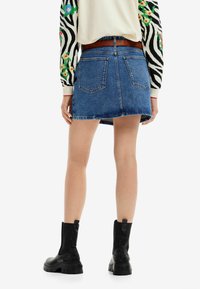 Džínová mini sukně s roztrhaným lemem, s zadními kapsami a pevným střihem. Nosit s černými kotníkovými botami a vzorovaným svetrem.