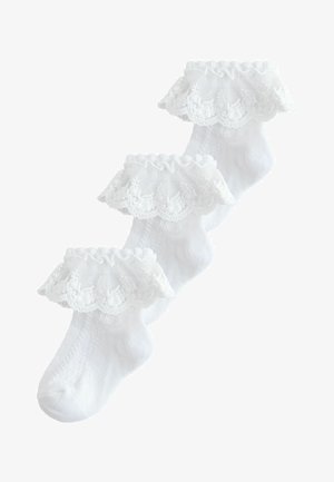 Drei weiße Baby-Socken mit zarten Spitzenrüschen rund um den Knöchel, überlappend auf einem weißen Hintergrund angeordnet.