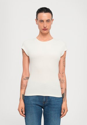 T-shirt ajusté à manches courtes en crème, en tissu côtelé. Doté d'un col rond et d'une texture lisse. Porté avec un jean en denim bleu.