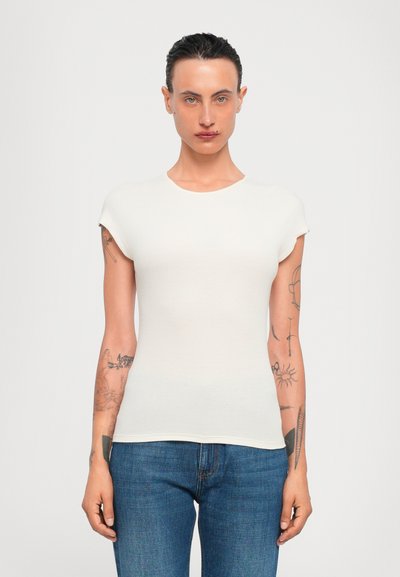 Figurbetontes T-Shirt mit kurzen Ärmeln in Creme, aus Rippstoff. Mit Rundhalsausschnitt und glatter Textur. Getragen mit blauen Jeans.