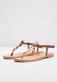 Ploché sandály s hnědým koženým páskem a látkou s zvířecím vzorem. Mají pantoflový design a hladkou, světle hnědou podrážku.