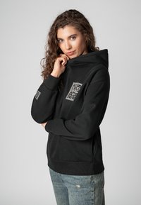 Zwarte trui met een hoge kraag en een zak aan de voorkant, met witte grafische ontwerpen op de borst en mouw. Zacht materiaal van katoenmix.