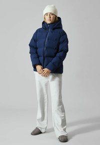 Marineblå vattert jakke med hette, med quiltet design. Kombinert med grå joggebukse og en hvit ribbestrikket lue. Mykt, avslappet utseende.