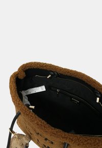 Borsa a tracolla marrone con texture, interno nero, tasca interna con zip visibile e portachiavi a forma di orsacchiotto attaccato.