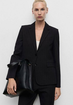 Černý pruhovaný blazer s ostrými klopami, se dvěma knoflíky a přední kapsou, doplněný velkou černou koženou taškou.