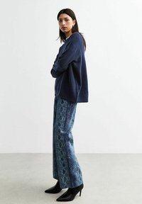Pull-over en maille bleu marine et pantalon large à motifs bleus avec un design en peau de serpent. Bottes à talons aiguilles noires.