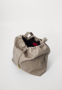 Saco de drawstring em couro taupe com detalhes dourados e etiqueta HUGO vermelha no interior, posicionado contra um fundo branco.