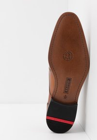 Brown leather shoe sole with a prominent embossed logo, curved design, and contrasting black rubber heel with a red accent stripe.