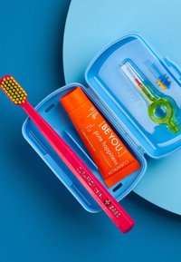 Une trousse de voyage bleue contenant une brosse à dents rose, un tube de dentifrice orange et un outil dentaire vert, tous disposés soigneusement.