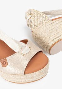 Sandalias de cuña de esparto beige con acabado de purpurina, punta abierta, detalles de tela trenzada y suela de cuerda de yute. Destalle de hardware en tono dorado.
