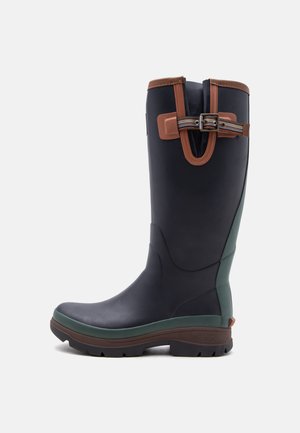 Botte haute en caoutchouc bleu foncé avec semelle marron et verte, bordure marron et sangle réglable rayée avec boucle près du haut.