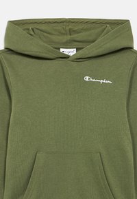 Φούτερ με κουκούλα σε ελιά πράσινο χρώμα, με κορδόνι για τη ρύθμιση της κουκούλας, εμπρόσθια τσέπη καγκουρό και κεντητό λευκό λογότυπο "Champion". Μαλακό, υφασμάτινο μείγμα βαμβακιού με υφή.