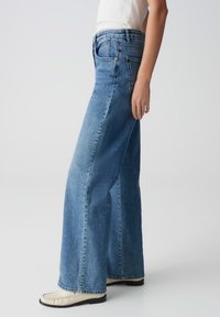 Wijduitlopende blauwe denim jeans met een hoge taille, voorzien van een klassiek vijf-pocket ontwerp en subtiele wassing, gecombineerd met beige loafers.