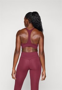 Burgundy athletic top with a racerback design, paired with matching high-waisted leggings. Smooth, stretchy material with seam detailing.
