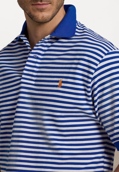 Modré a bílé pruhované polo tričko se š solidní modrou límcem a malým oranžovým logem na levé straně. Krátké rukávy a měkká textura látky.