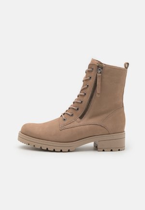 Stivale ankle in suede beige con chiusura a lacci davanti, cerniera laterale e suola robusta e testurizzata; presenta una punta tonda e un leggero tacco a blocco.