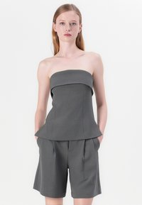 Gråtte strapless topp med en strukturert peplum-design, kombinert med løstsittende grå shorts med sidelommer og subtile plissee detaljer.