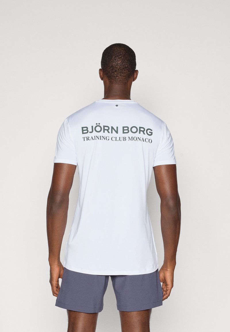 Λευκό αθλητικό μπλουζάκι κοντομάνικο με σκούρο πράσινο κείμενο στην πλάτη: "BJÖRN BORG" και "TRAINING CLUB MONACO". Λείο ύφασμα, εφαρμοστή σχεδίαση.