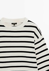 Pull en maille blanche côtelée avec des rayures noires horizontales et un col rond, montrant le haut du torse et la manche droite.