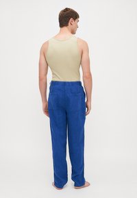 Blå linbukser med en løs pasform, med elastisk talje og to baglommer, parret med en beige tanktop.