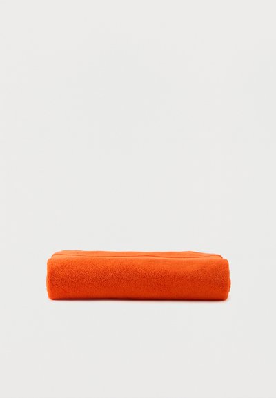 Φωτεινή πορτοκαλί διπλωμένη πετσέτα με ορατή υφή τοποθετημένη σε απλό ανοιχτό γκρι φόντο.