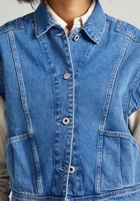 Giubbotto di jeans di colore azzurro chiaro con chiusura a bottoni, due tasche laterali, cuciture in contrasto e colletto.