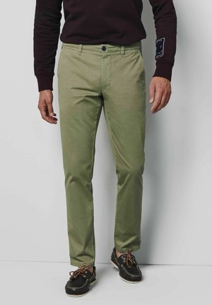 Licht olijfgroene chinos met een rechte pasvorm, voorzien van een knoopsluiting en voorzakken, gecombineerd met zwarte bootsschoenen en een donkere trui.