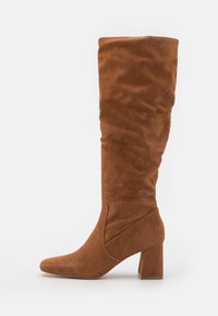 Bota de ante marrón hasta la rodilla con tacón cuadrado y punta afilada, que presenta una suave textura caída en el eje.