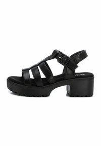 Sandalias de tacón de cuero negro con múltiples correas, una suela texturizada gruesa y una hebilla en el tobillo ajustable para un ajuste seguro.