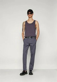 Pilkas tankinis marškinėlis, pilkos kelnės ir juodi batai. Modelis dėvi saulės akinius ir juodą kepurę. Paprastas dizainas su laisvu, kasdienišku stiliumi.