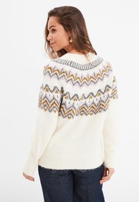 Weißer Strickpullover mit einem gemusterten Yoke in Grautönen, Gold und Rosa. Verfügt über gerippte Bündchen und Saum sowie eine lockere Passform.