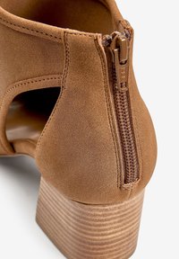 Bottine en suède marron avec une fermeture éclair latérale, un talon empilé texturé et un design découpé pour la ventilation.