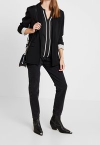 Svart kavaj över en svartvit randig blus, tillsammans med svarta jeans och svarta ankelstövlar med spetsiga tår. En enkel handväska.