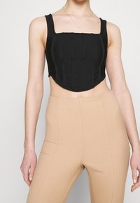 Černý zkrácený top se strukturovaným trupem, čtvercovým výstřihem a širokými ramínky. Má vertikální švy a mírně zaoblený spodní lem.