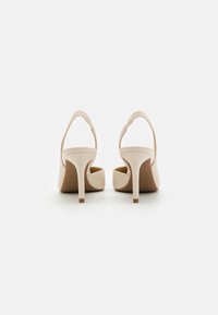 Beige högklackade slingback-skor med en slät yta, rundade kanter och en tunn klack som inkluderar ett band över hälen.